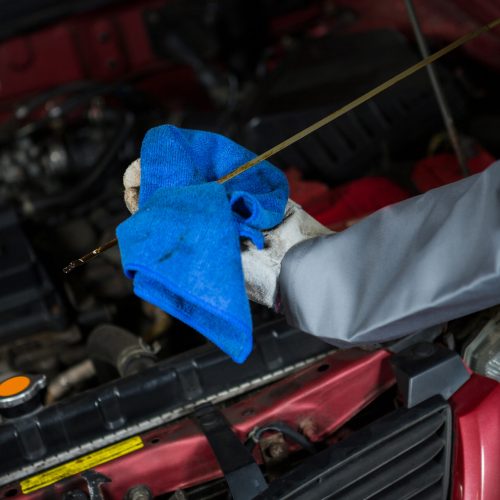 Mechanic checking the oil level in a car engine with a dipstick at repair garage